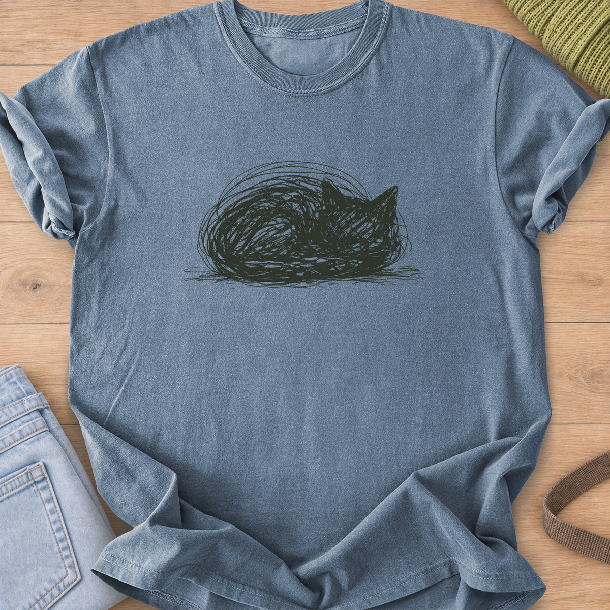 Scribbled cat curled into a round loaf with ears poking up, dark charcoal ink on a Blue Jean T-Shirt