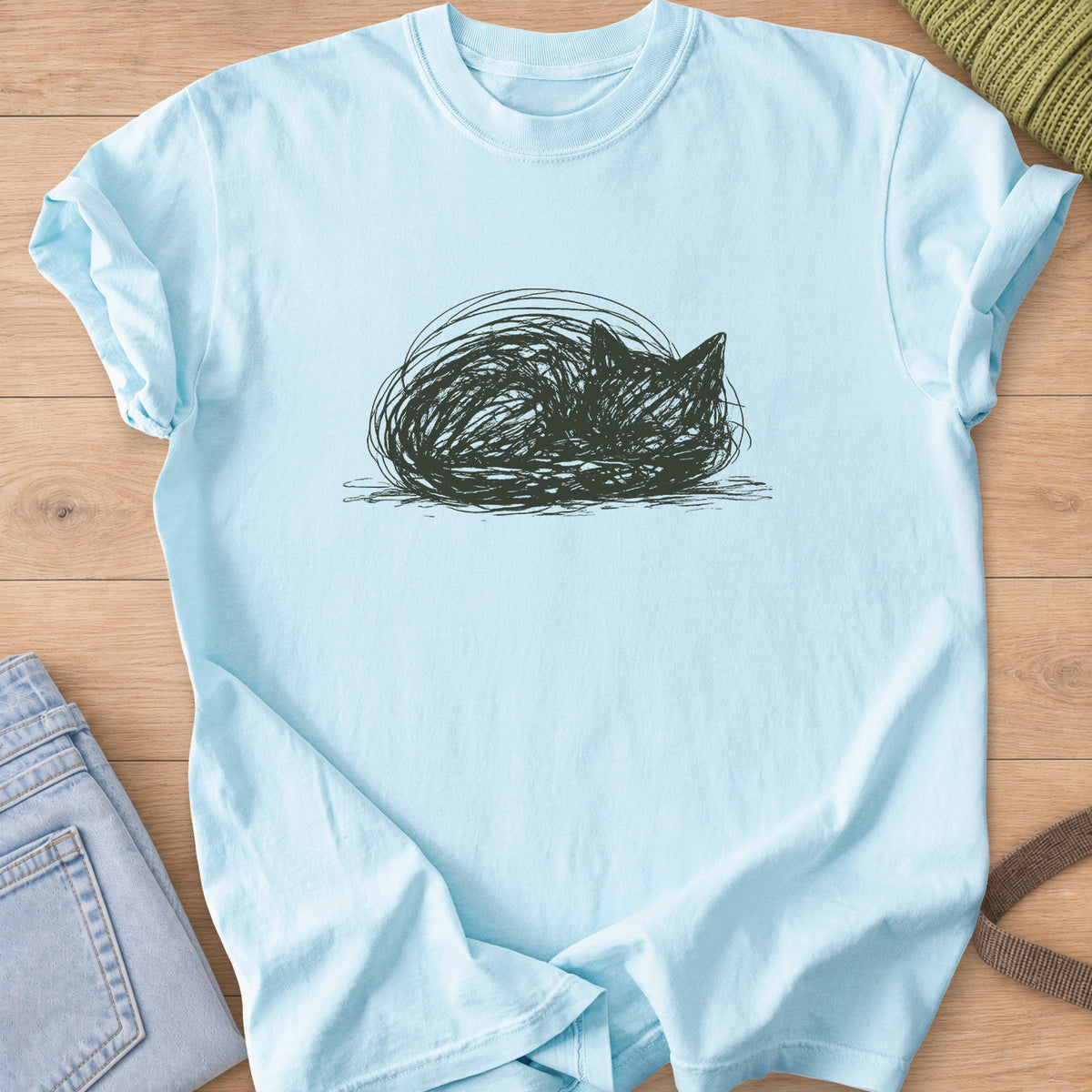 Scribbled cat curled into a round loaf with ears poking up, dark charcoal ink on a Chambray T-Shirt