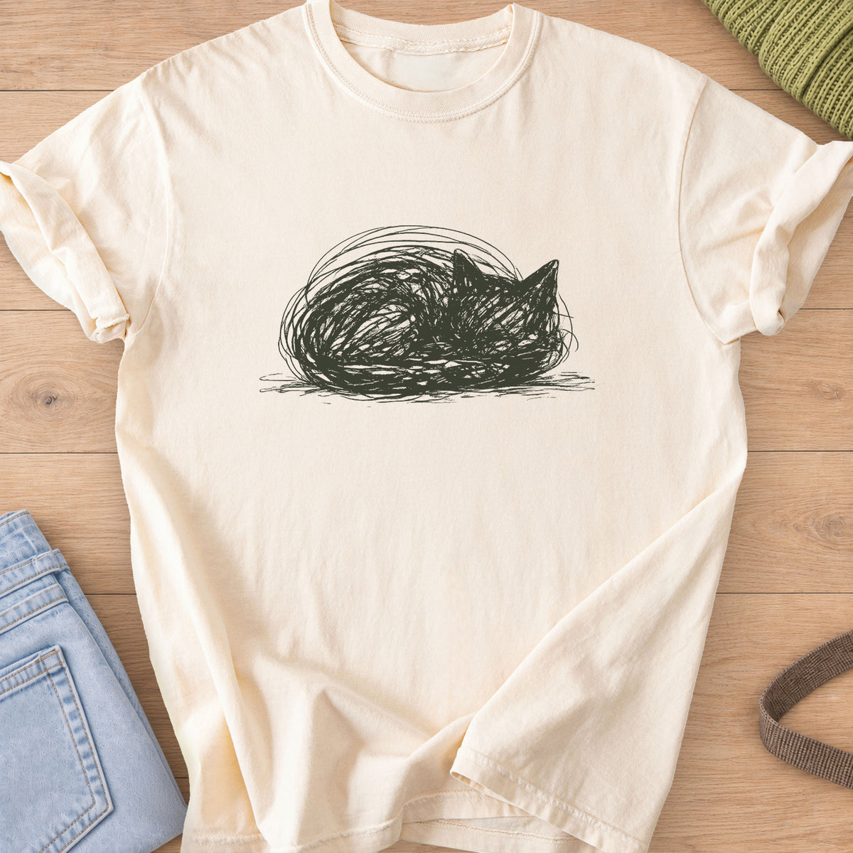 Scribbled cat curled into a round loaf with ears poking up, dark charcoal ink on an Ivory T-Shirt