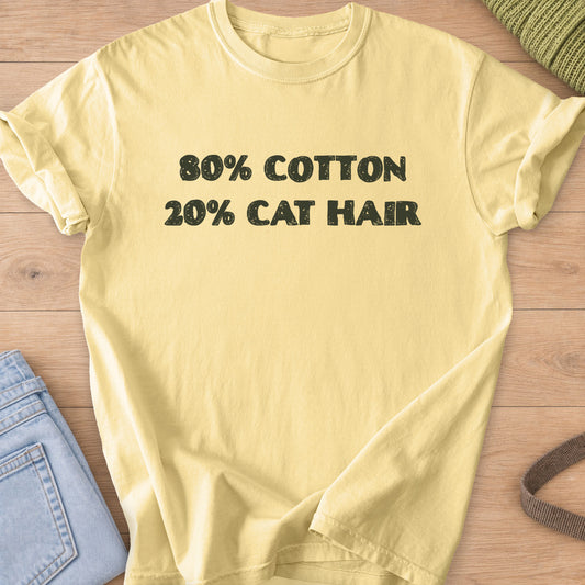 Distressed block letters that read "80% COTTON 20% CAT HAIR", dark charcoal ink on a Butter T-Shirt