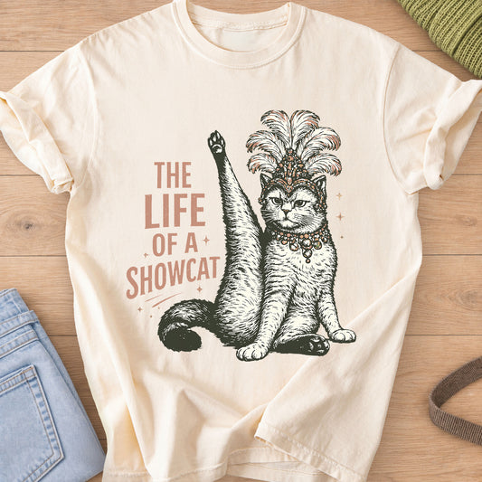 Cat in a feathered showgirl headdress raises one leg high, "The Life of a Showcat" on an Ivory T-Shirt