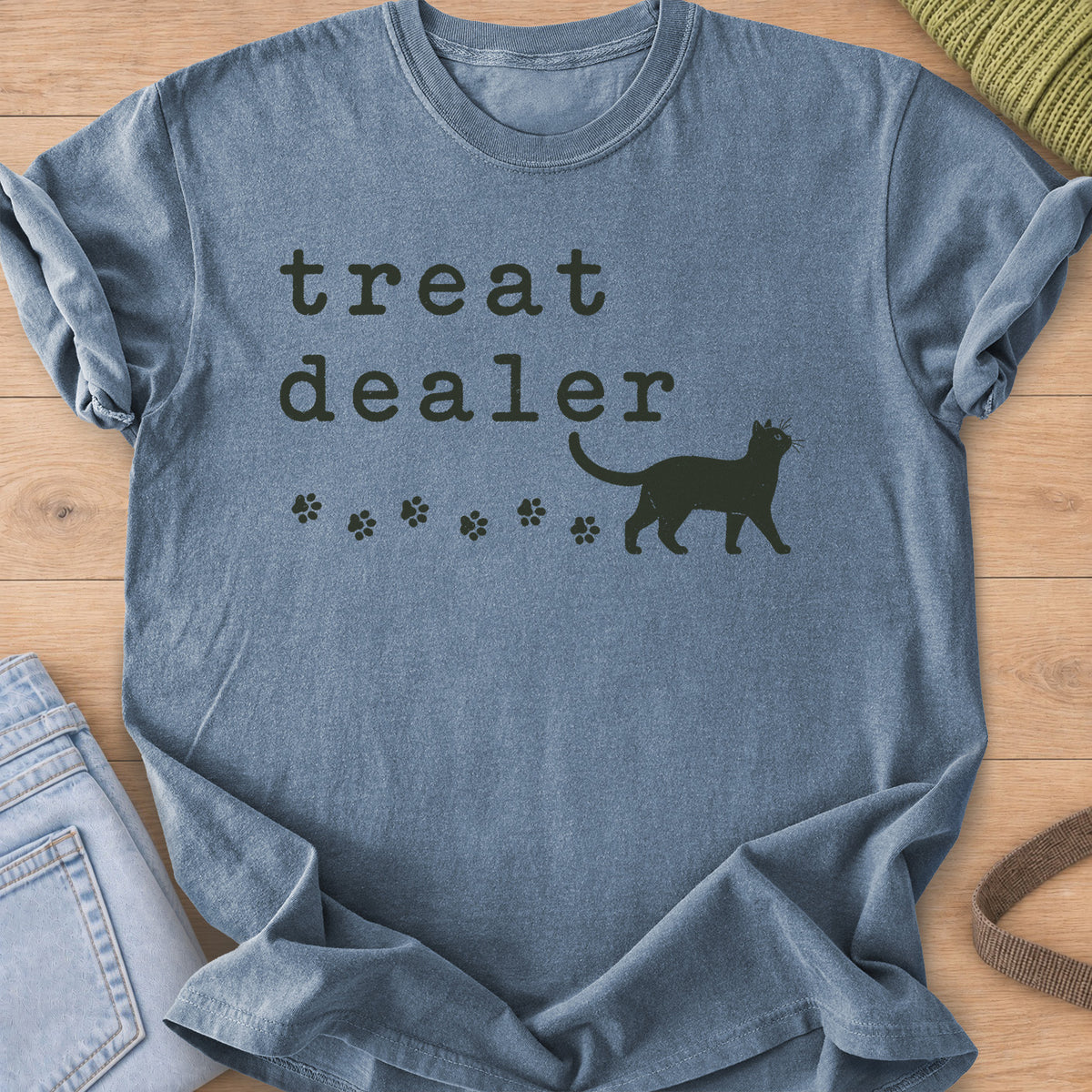Walking cat silhouette with a trail of paw prints beneath the words "treat dealer", dark charcoal ink on a Blue Jean T-Shirt