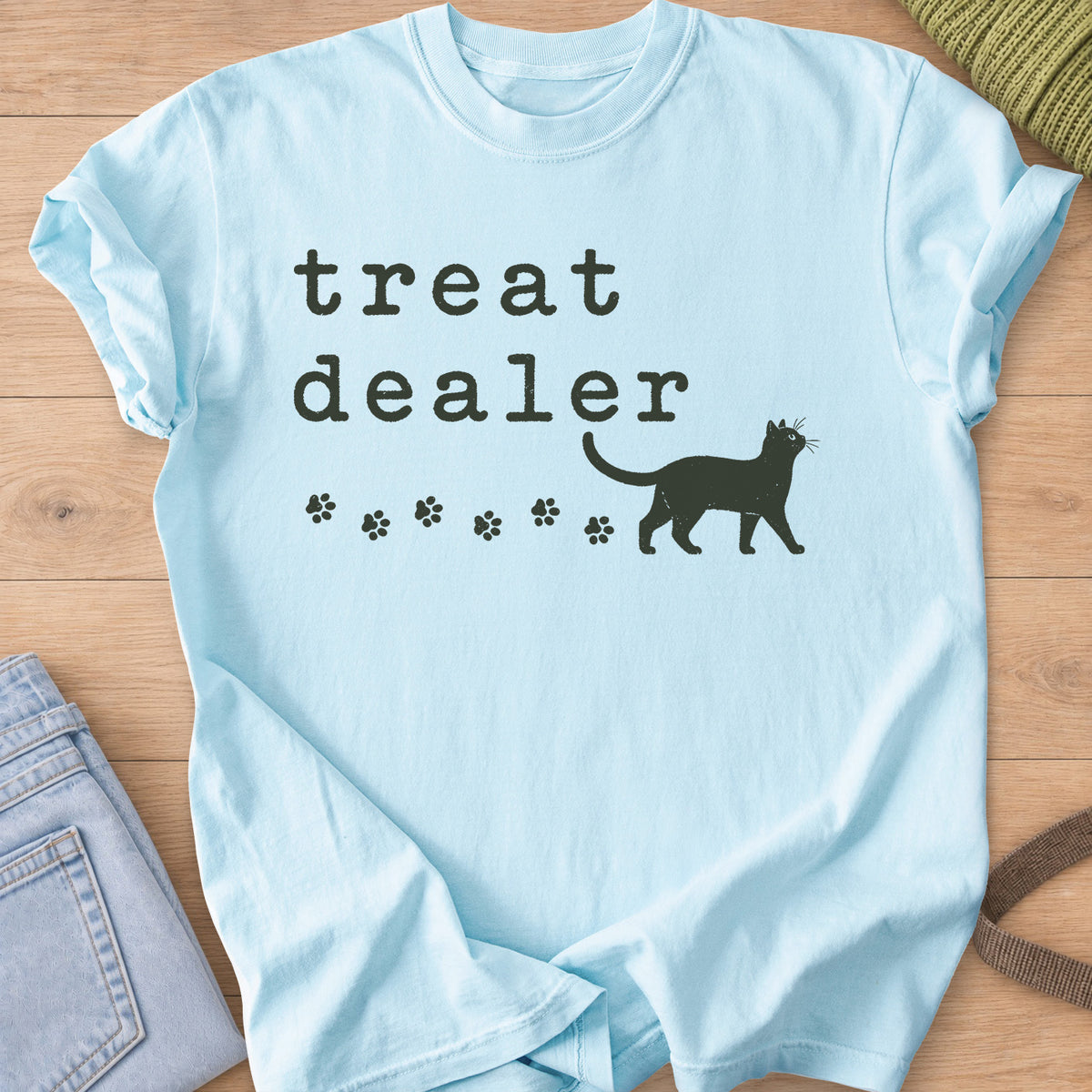 Walking cat silhouette with a trail of paw prints beneath the words "treat dealer", dark charcoal ink on a Chambray T-Shirt