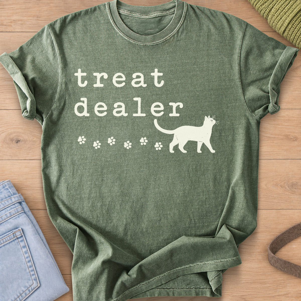 Walking cat silhouette with a trail of paw prints beneath the words "treat dealer", cream ink on a Moss T-Shirt