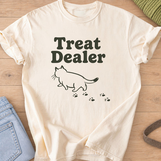 Chubby cat outline walking away under "Treat Dealer" with a trail of paw prints, dark charcoal ink on an Ivory T-Shirt