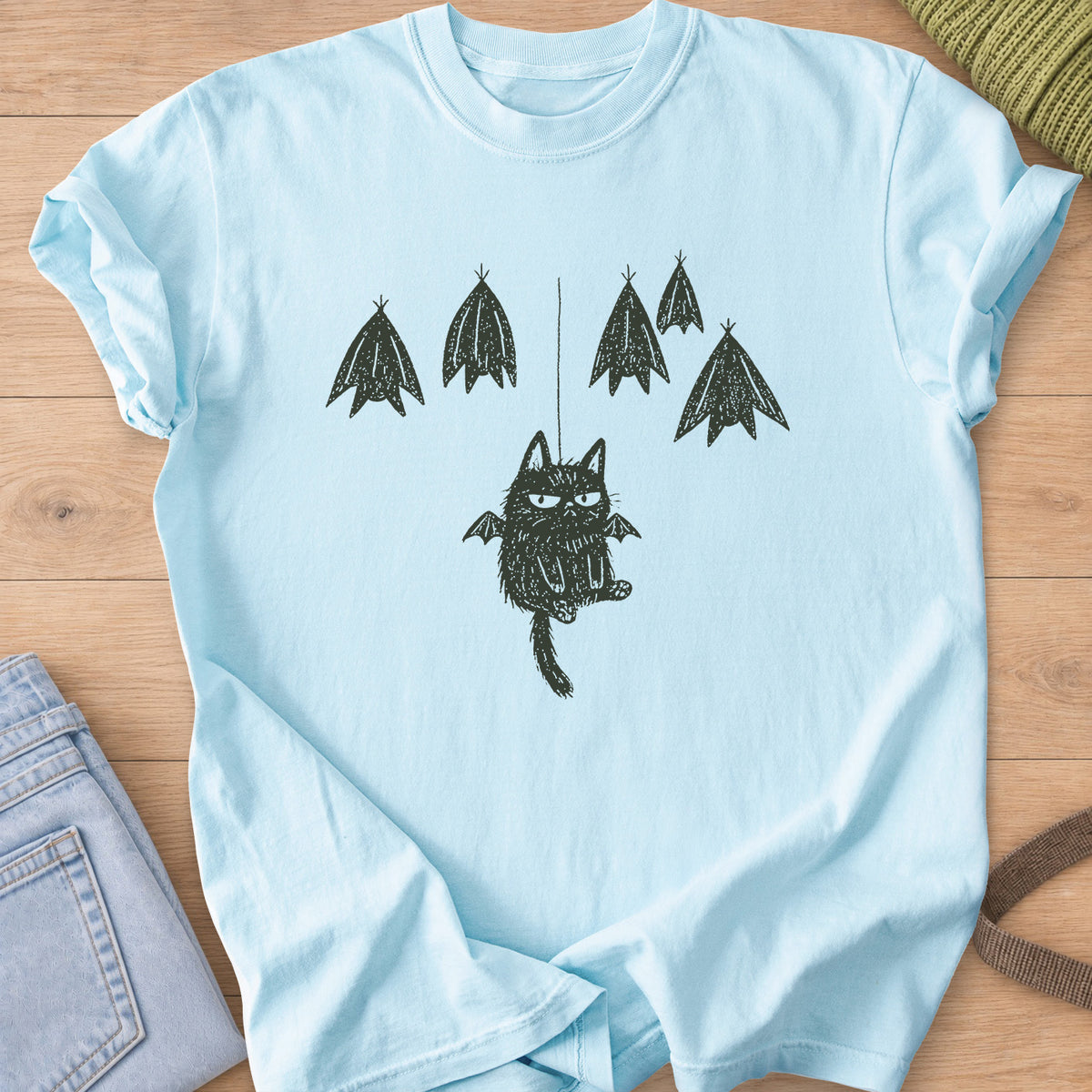 Grumpy fuzzy cat with bat wings dangling from a string among roosting bats, dark charcoal ink on a Chambray T-Shirt