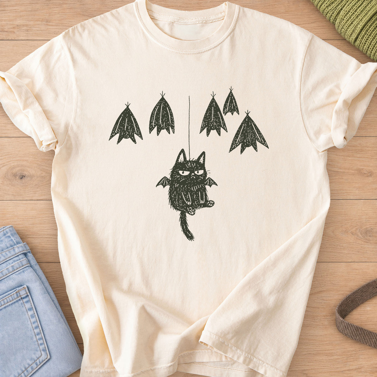 Grumpy fuzzy cat with bat wings dangling from a string among roosting bats, dark charcoal ink on an Ivory T-Shirt