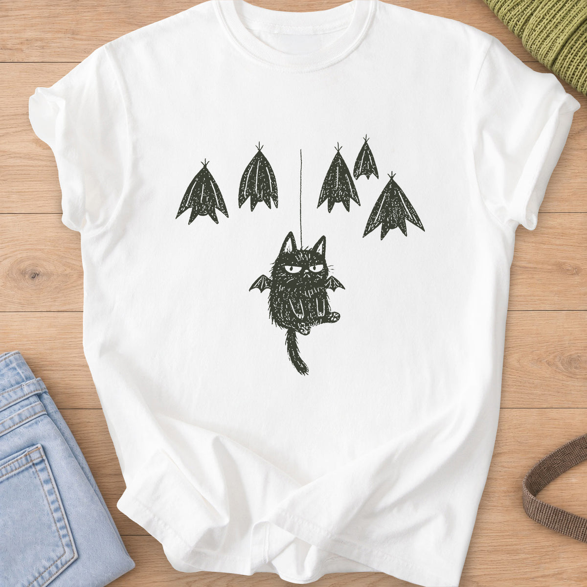 Grumpy fuzzy cat with bat wings dangling from a string among roosting bats, dark charcoal ink on a White T-Shirt
