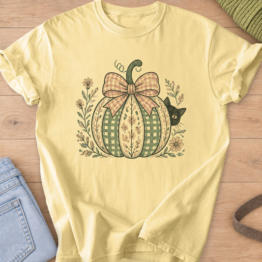 Black cat peeking from behind a gingham pumpkin with a big bow and wildflowers on a Butter T-Shirt