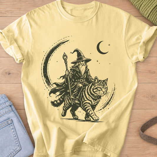 Bearded wizard with a staff riding a big striped cat under a crescent moon, dark charcoal ink on a Butter T-Shirt