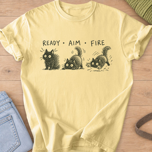 Three wide-eyed fluffy cats sit, crouch and pounce under "Ready Aim Fire", dark charcoal ink on a Butter T-Shirt