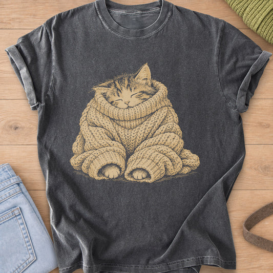 Sleeping tabby kitten bundled in an oversized cable-knit sweater, paws peeking out, tan ink on a Pepper T-Shirt