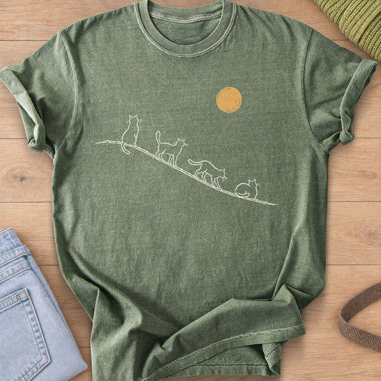 Four cats sit, walk and curl up along a sloping rooftop under a full moon, cream and gold ink on a Moss T-Shirt