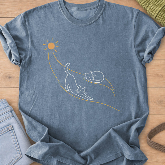 Two cats, one stretching and one curled up asleep, on sunbeams flowing from a sun, white and gold ink on a Blue Jean T-Shirt