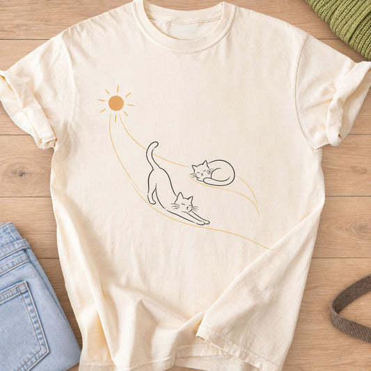 Two cats, one stretching and one curled up asleep, on sunbeams flowing from a sun, charcoal and gold ink on an Ivory T-Shirt