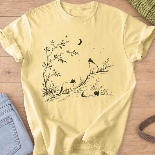 Three cats walking, sitting and sleeping on a hill by a tree under a crescent moon, dark charcoal ink on a Butter T-Shirt