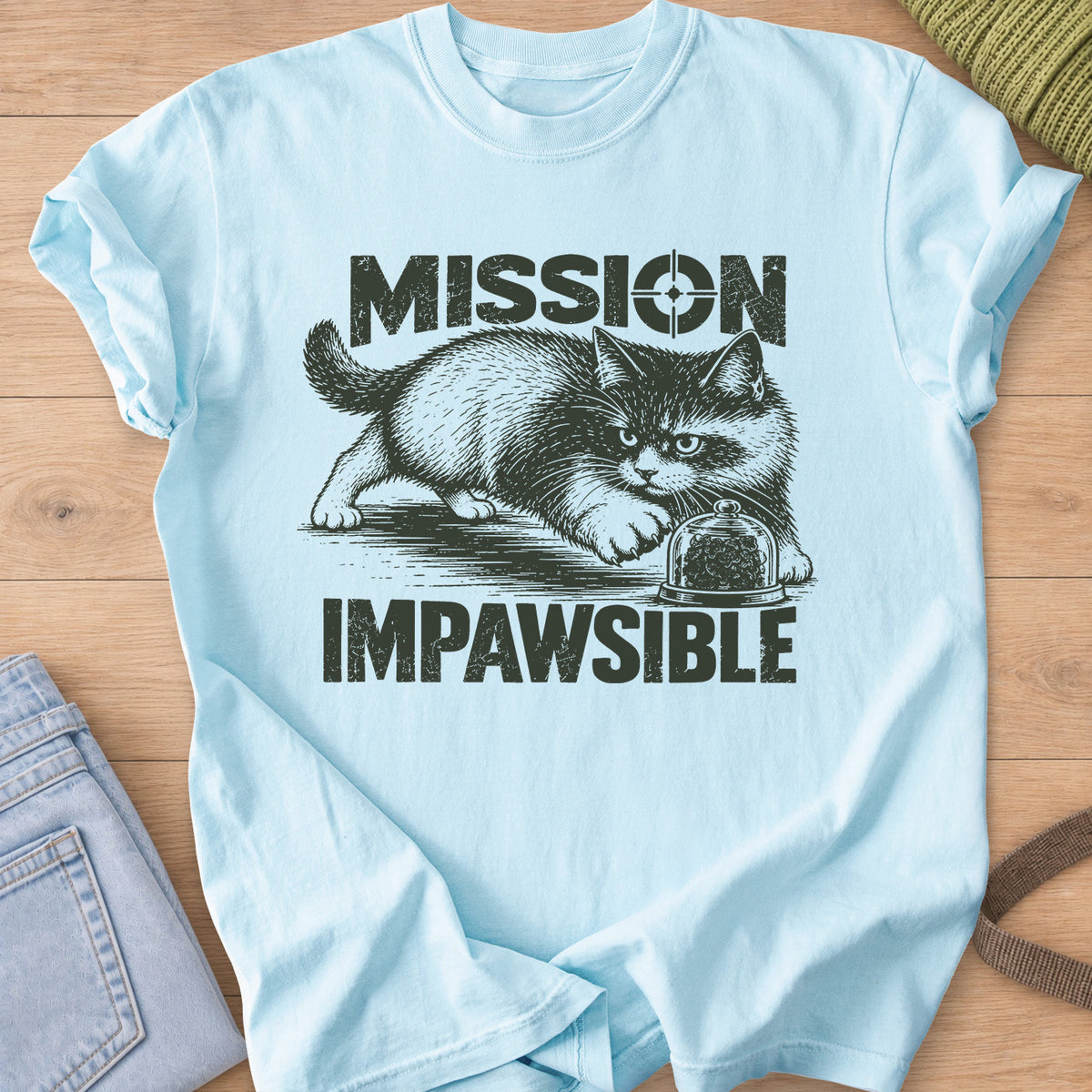 Fluffy cat sneaking toward a glass dome of treats under "Mission Impawsible", dark charcoal ink on a Chambray T-Shirt