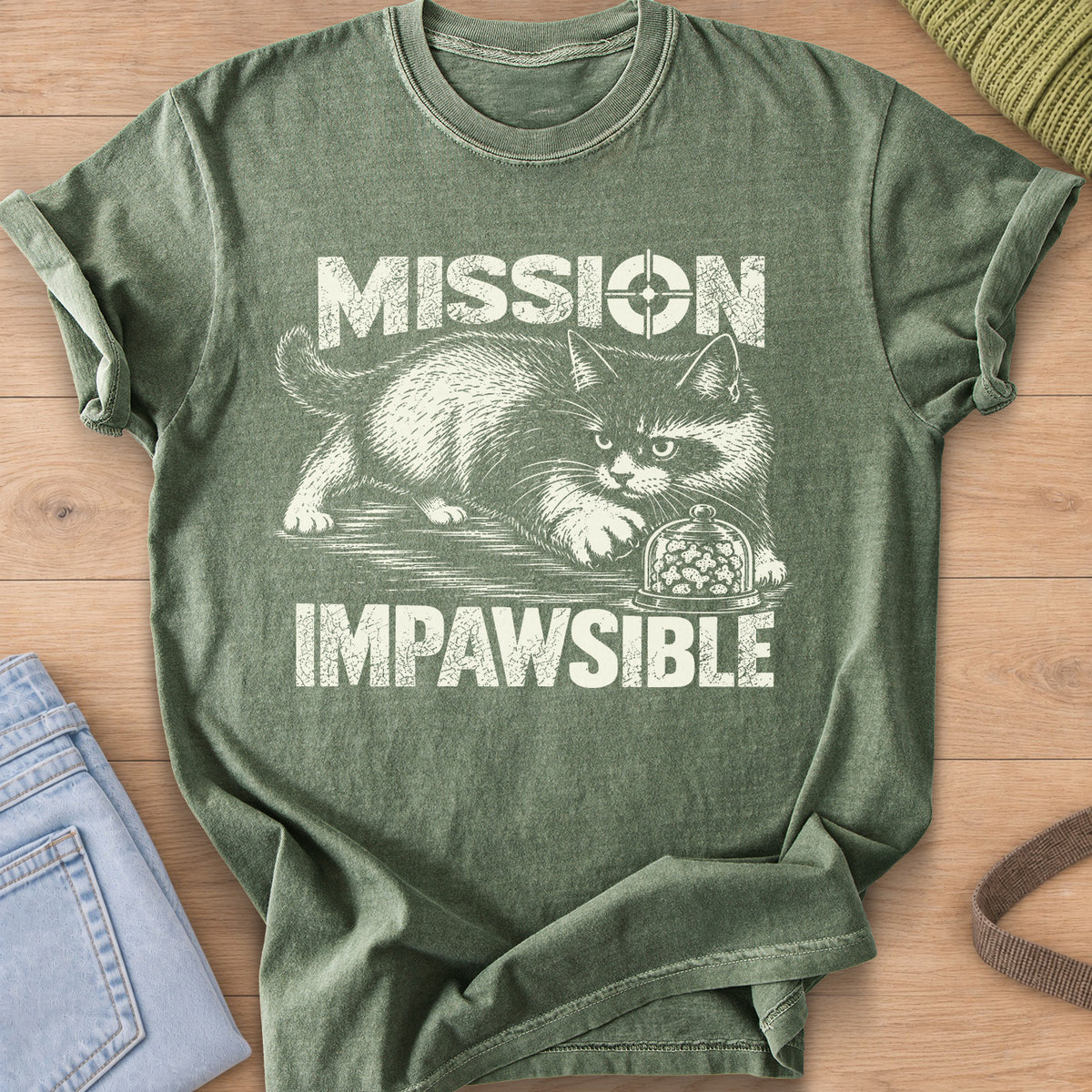 Fluffy cat sneaking toward a glass dome of treats under "Mission Impawsible", cream ink on a Moss T-Shirt