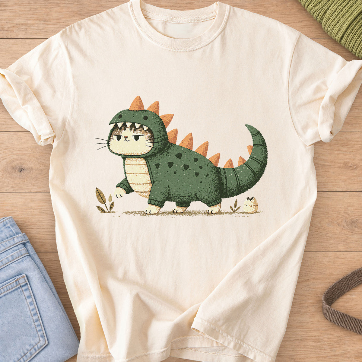 Grumpy cat in a spiky dinosaur costume walking past sprouts and a hatching egg on an Ivory T-Shirt