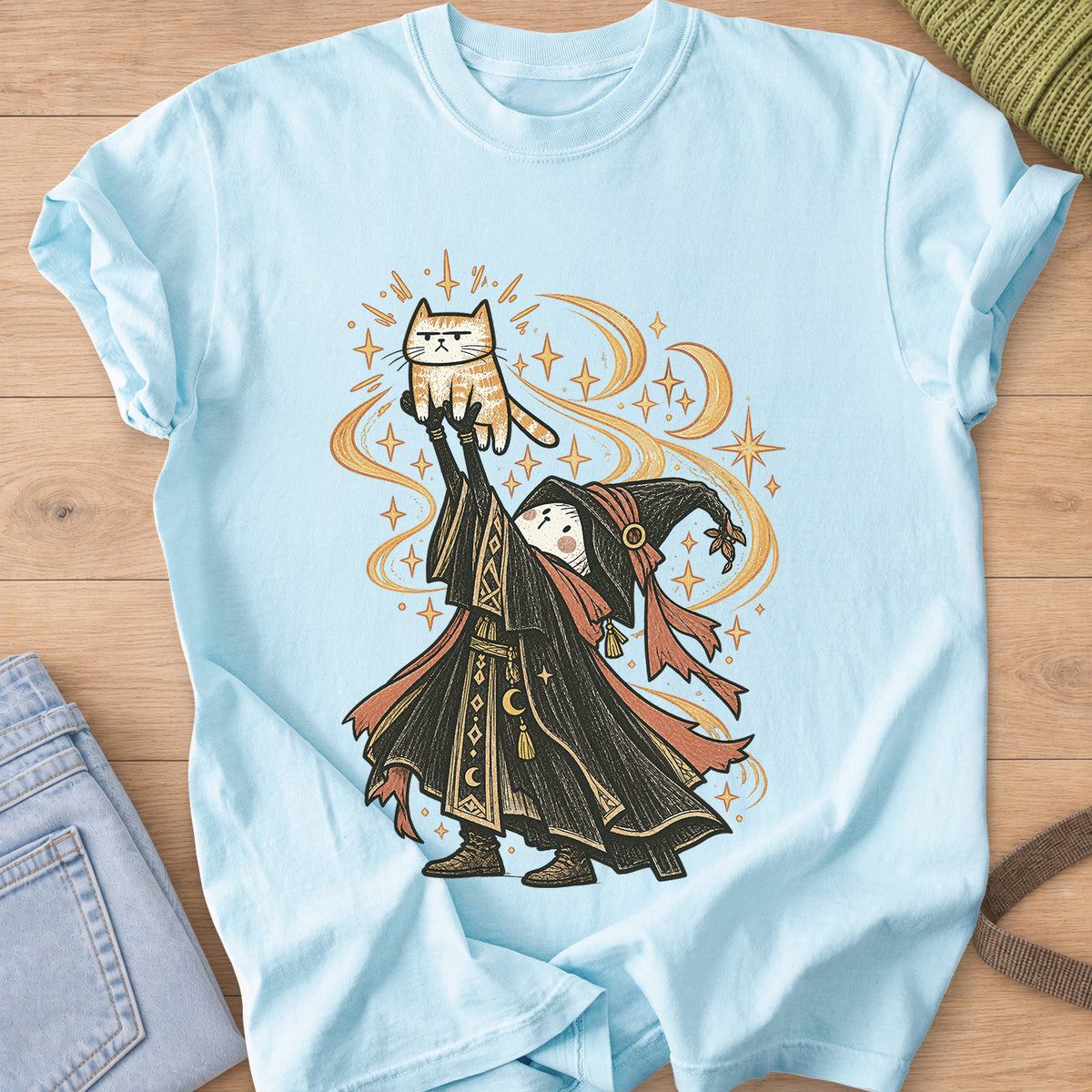 Robed wizard holds a grumpy tabby cat high overhead amid swirling stars and moons on a Chambray T-Shirt