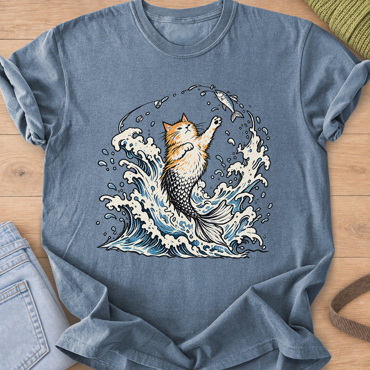 Fluffy cat with a mermaid tail rising from crashing waves, pawing at a hooked fish on a Blue Jean T-Shirt