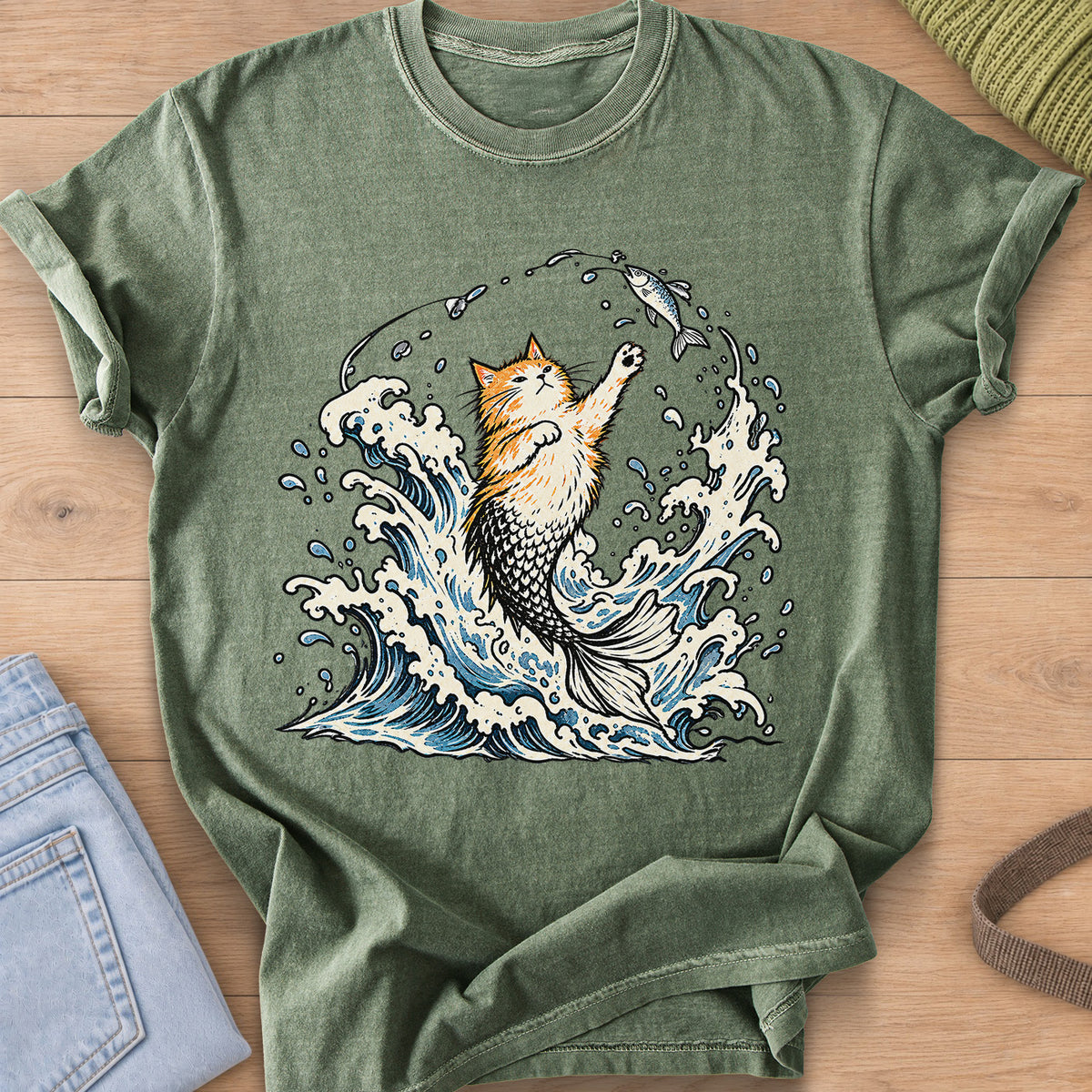 Fluffy cat with a mermaid tail rising from crashing waves, pawing at a hooked fish on a Moss T-Shirt