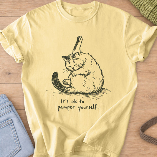 Fluffy cat grooming with one hind leg up in the air, "It's ok to pamper yourself.", dark charcoal ink on a Butter T-Shirt