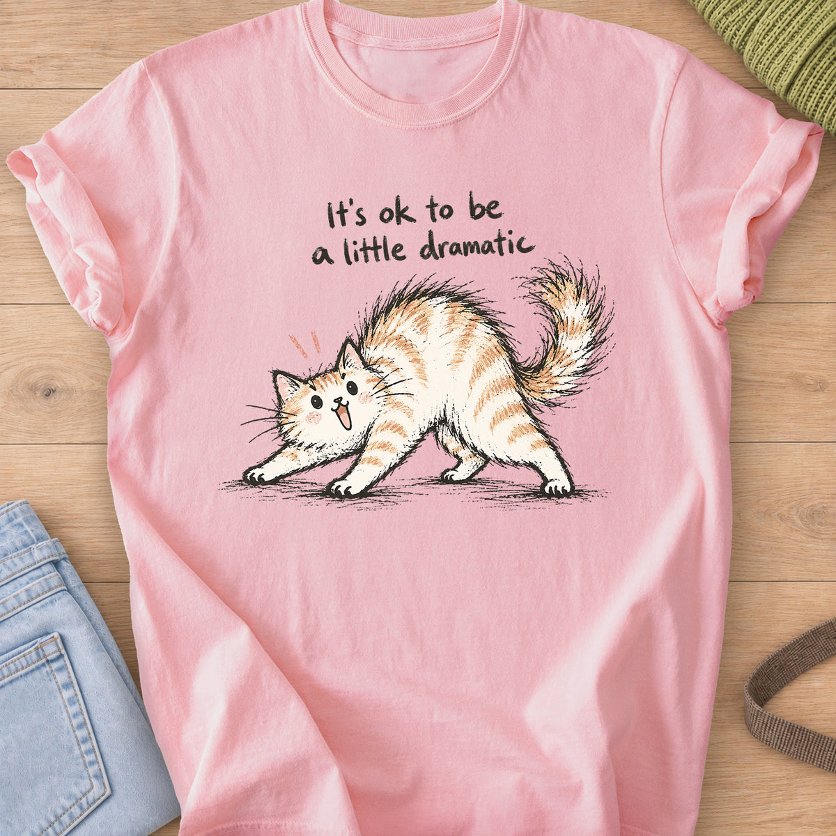 Startled fluffy cat arching its back beneath "It's ok to be a little dramatic" on a Blossom T-Shirt