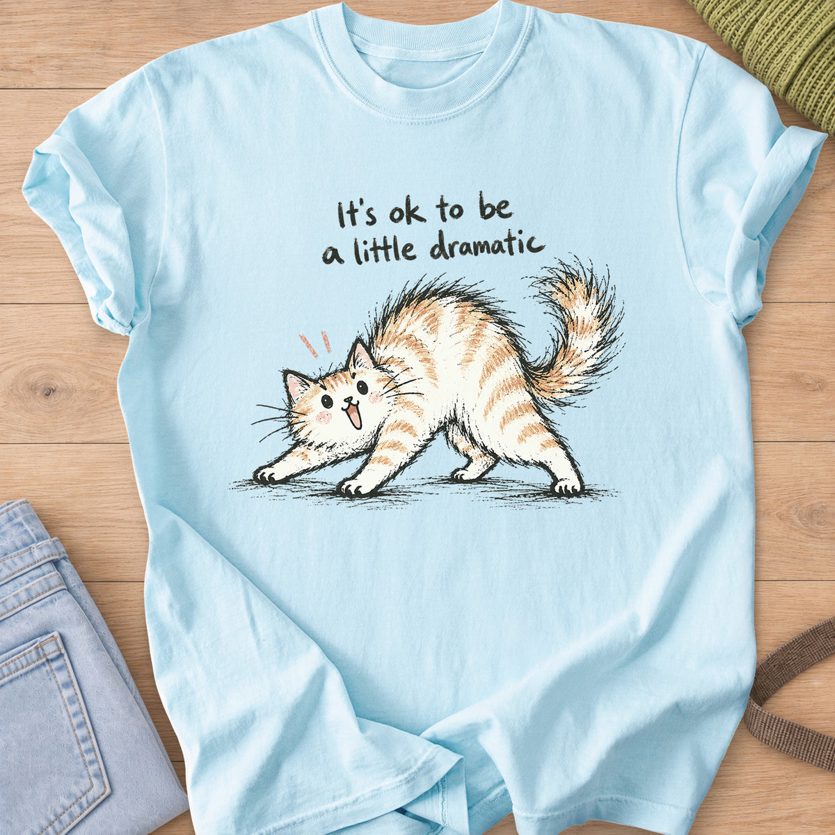 Startled fluffy cat arching its back beneath "It's ok to be a little dramatic" on a Chambray T-Shirt