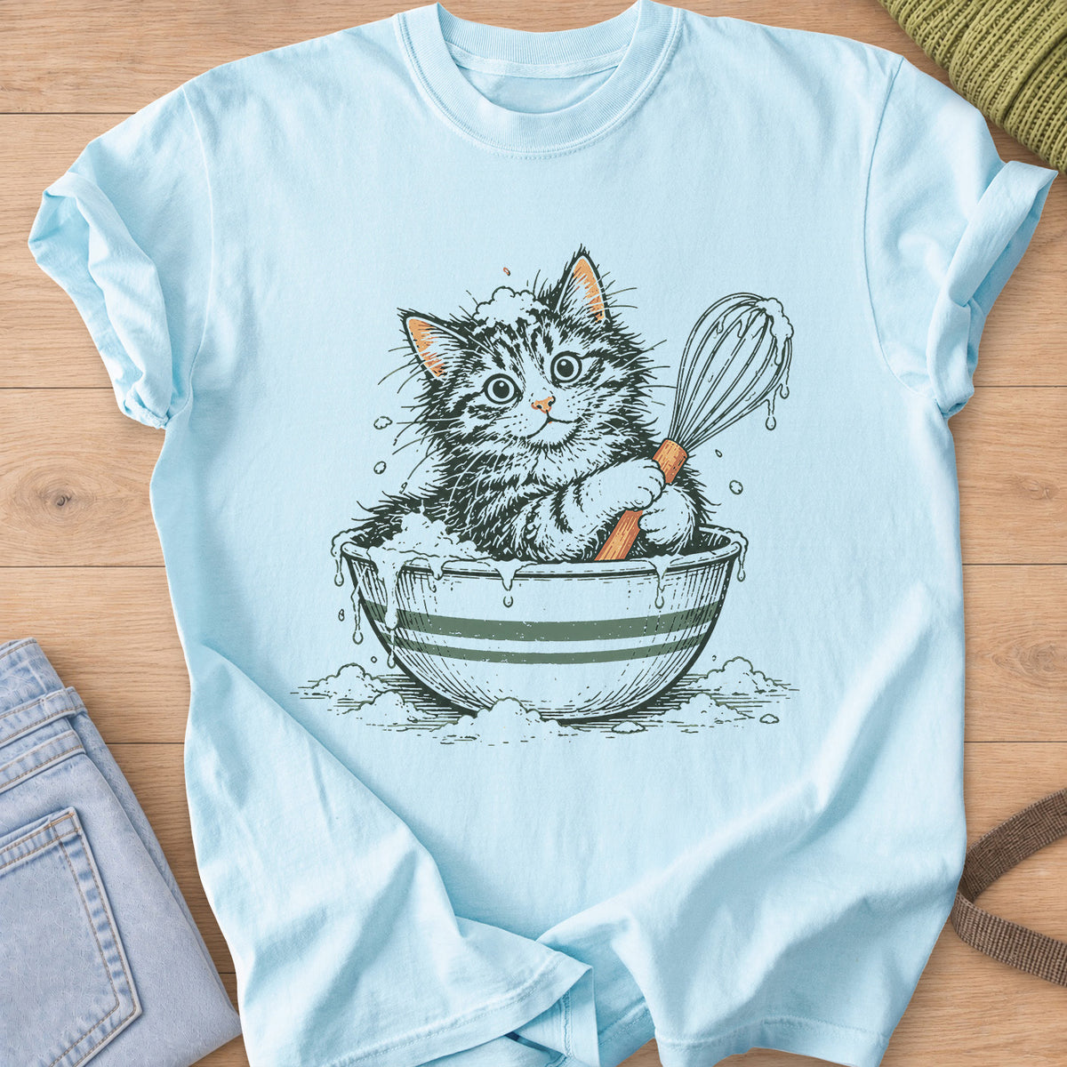 Tabby kitten sitting in a striped mixing bowl of batter, holding a dripping whisk on a Chambray T-Shirt