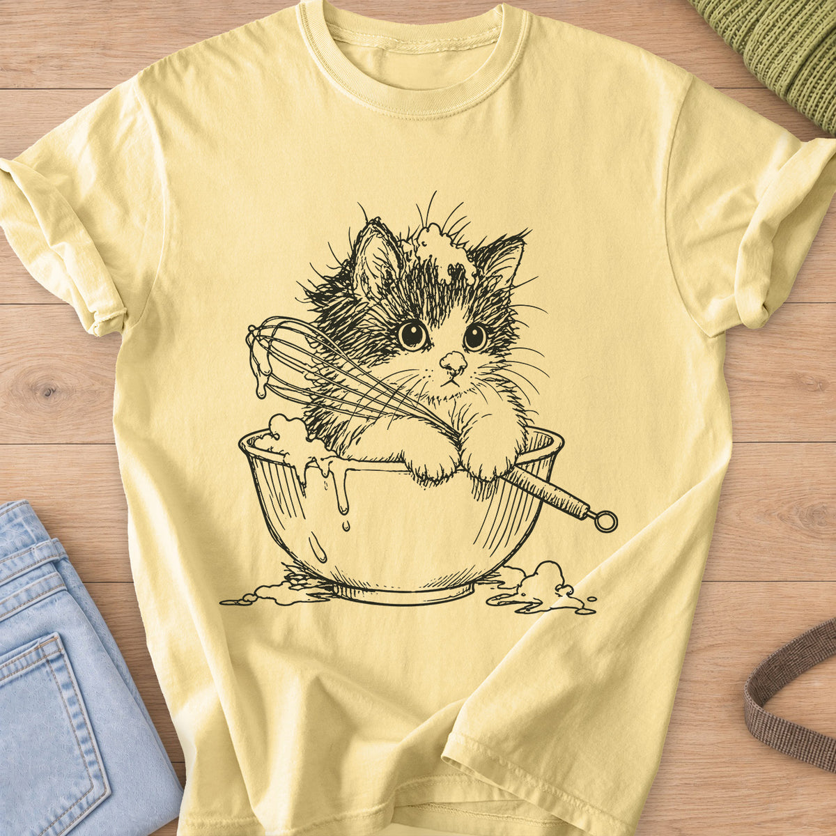 Fluffy kitten in a mixing bowl holding a whisk, with batter dripping over the side, black ink on a Butter T-Shirt