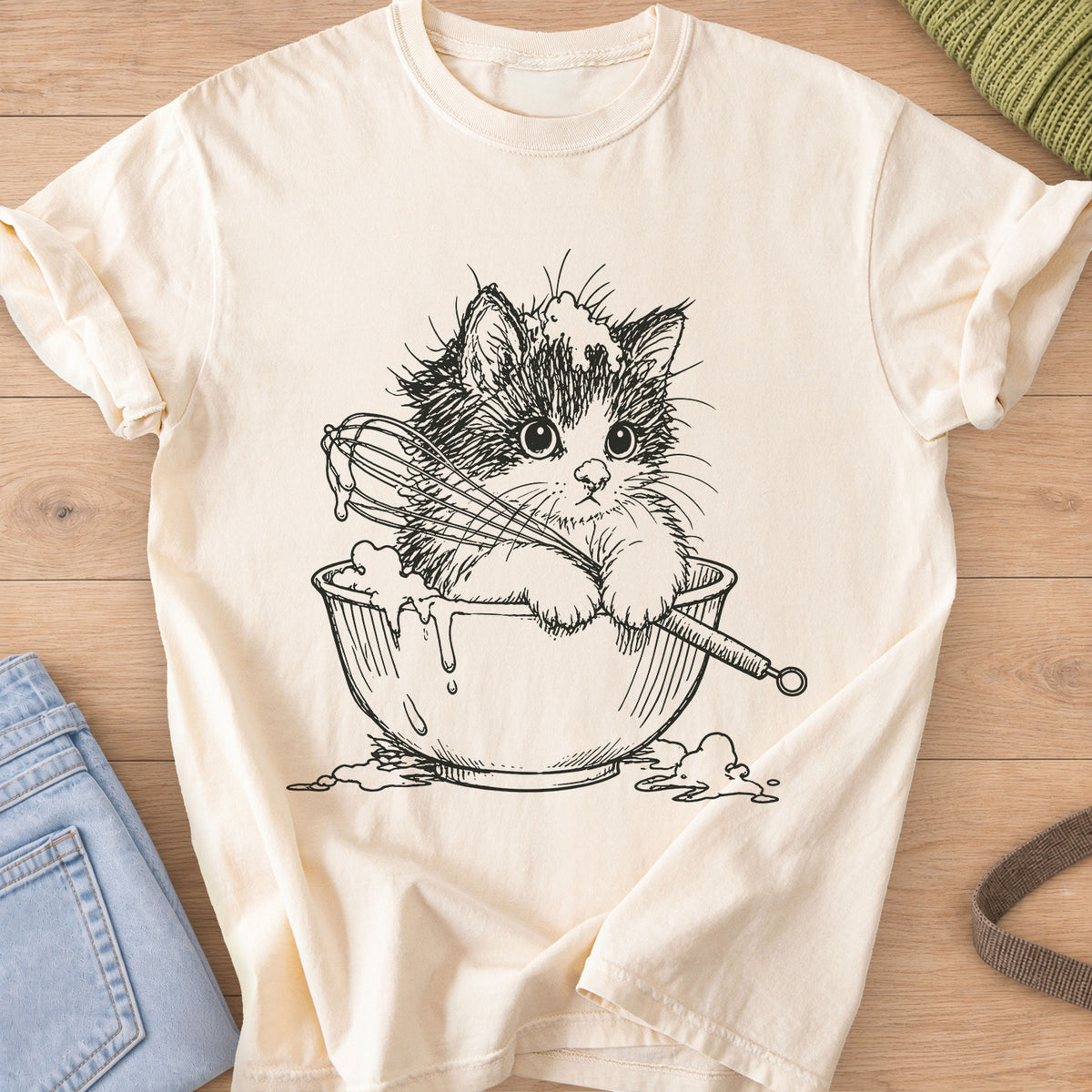 Fluffy kitten in a mixing bowl holding a whisk, with batter dripping over the side, black ink on an Ivory T-Shirt