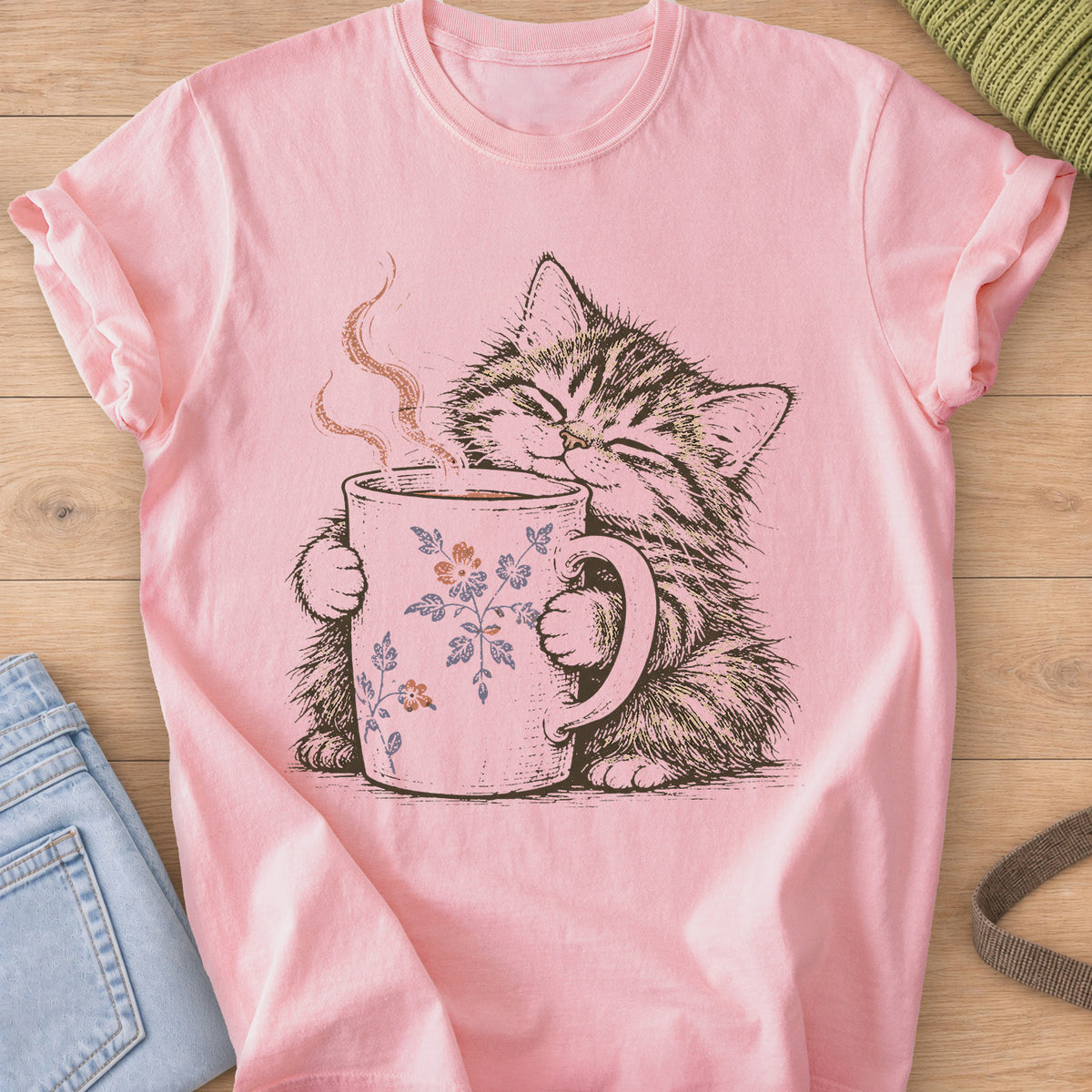Tabby kitten with closed eyes hugging a steaming mug painted with small flowers on a Blossom T-Shirt