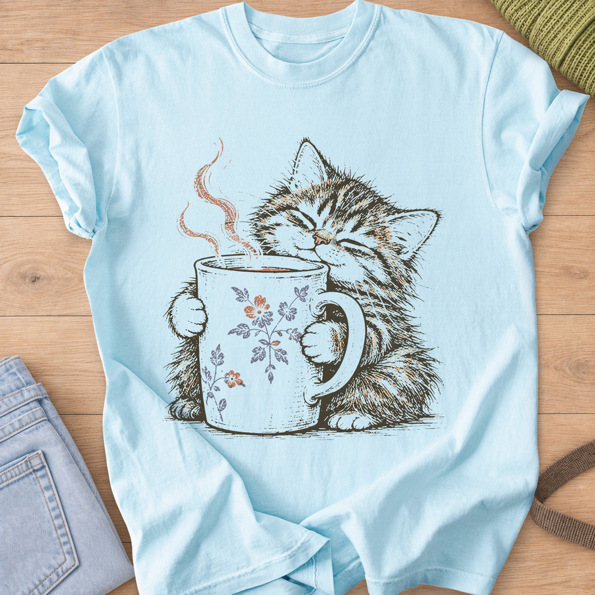 Tabby kitten with closed eyes hugging a steaming mug painted with small flowers on a Chambray T-Shirt
