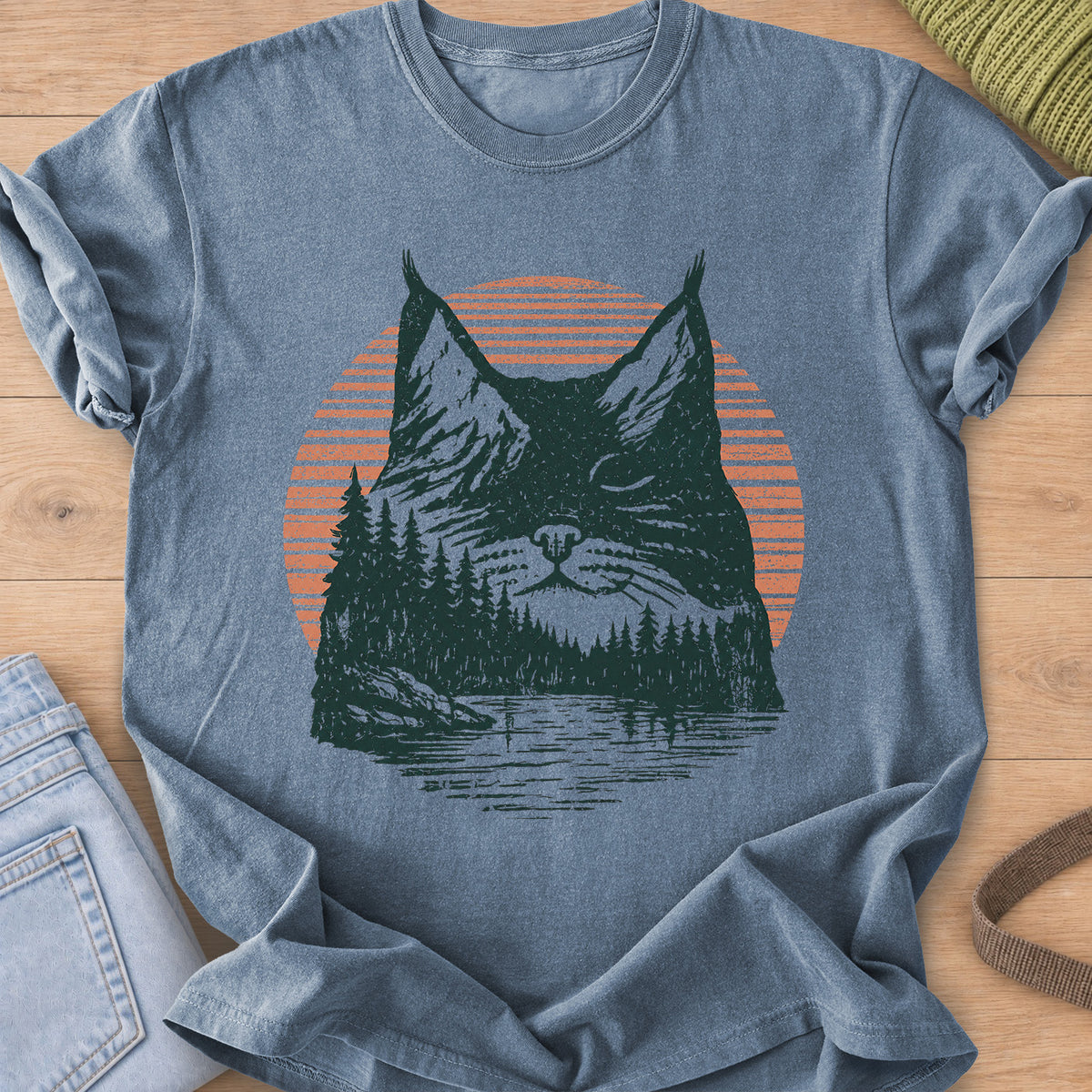 Cat face with closed eyes filled with mountains, pines, a lake and sun, dark green and coral ink on a Blue Jean T-Shirt