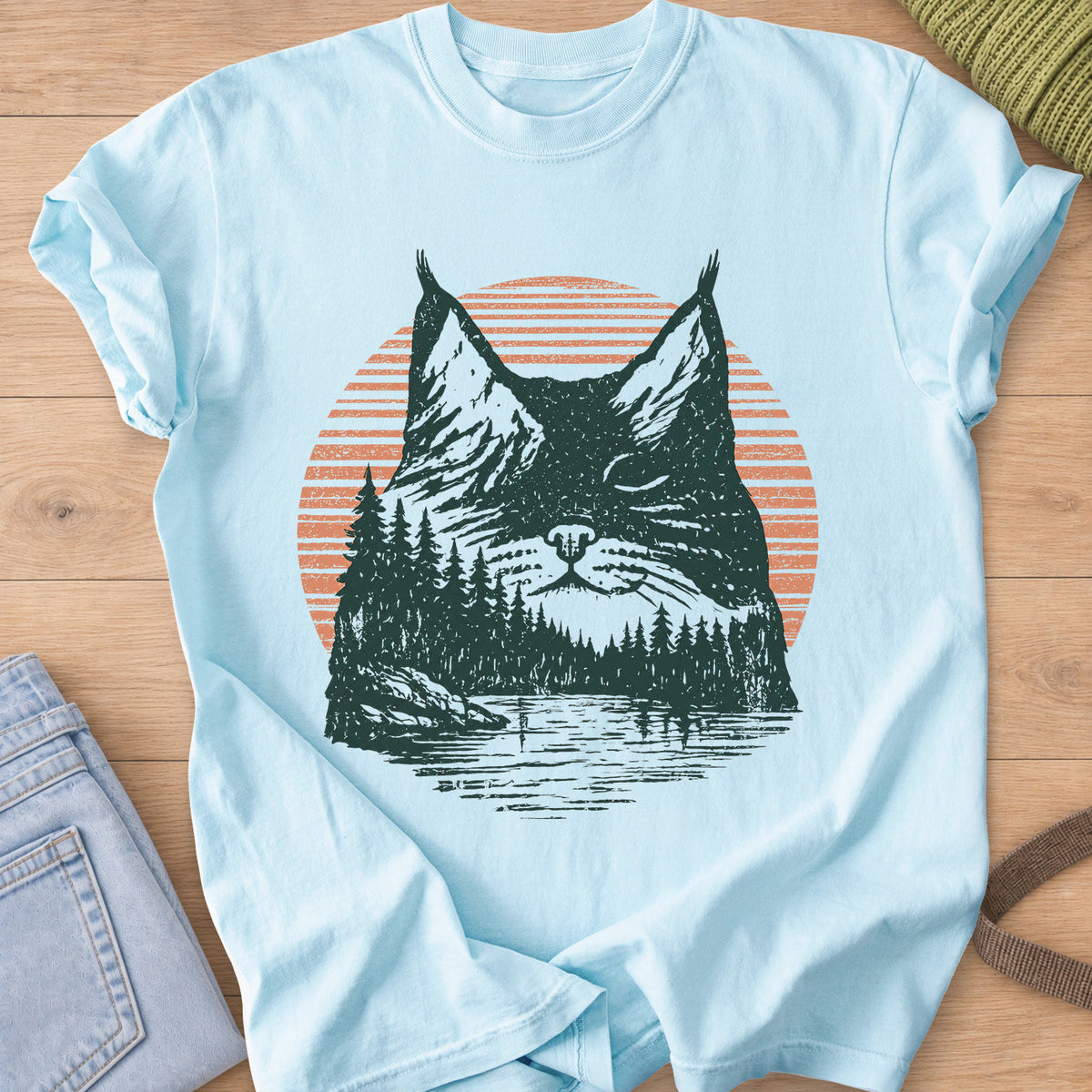 Cat face with closed eyes filled with mountains, pines, a lake and sun, dark green and coral ink on a Chambray T-Shirt