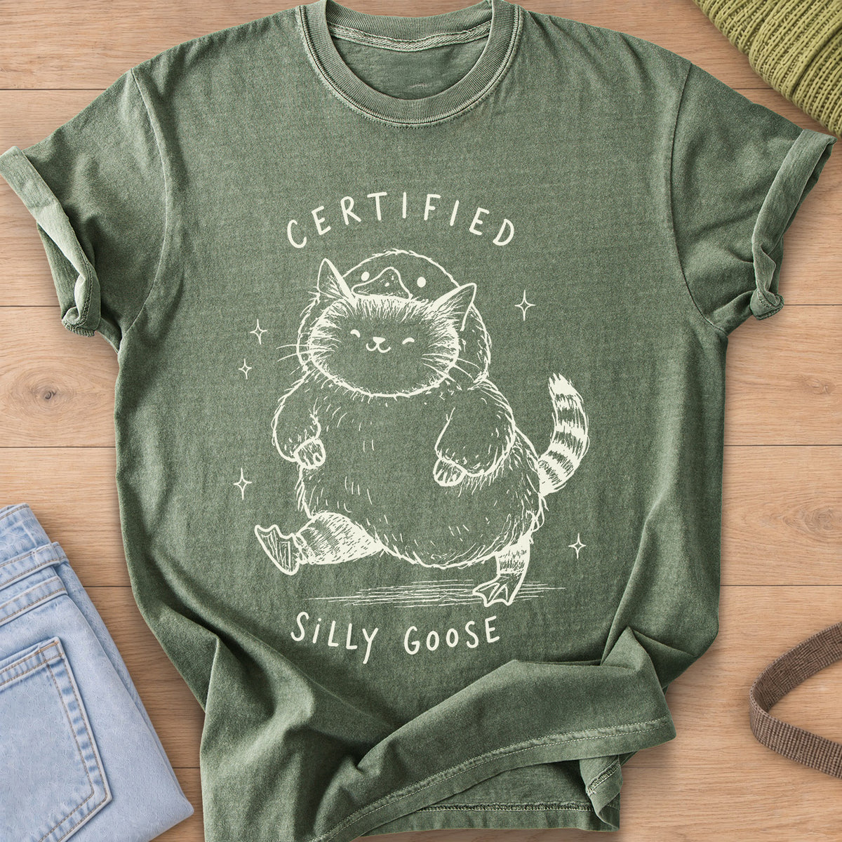 Chubby tabby cat in a goose costume walking among sparkles, "Certified Silly Goose", cream ink on a Moss T-Shirt