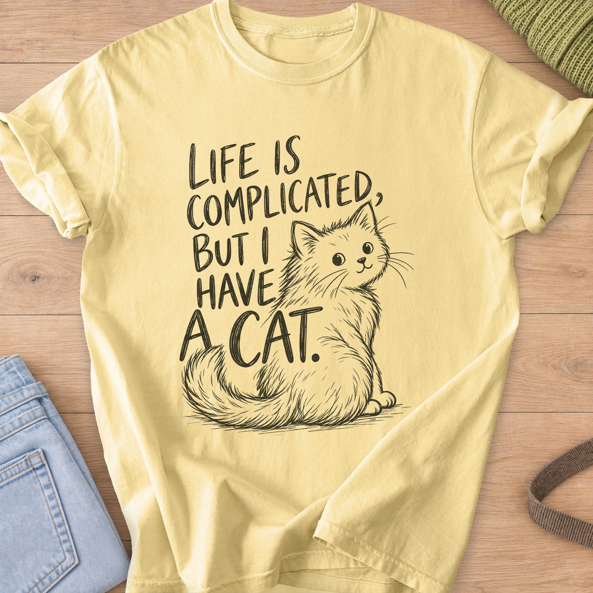 Fluffy cat sits and looks back beside "Life is complicated, but I have a cat.", dark charcoal ink on a Butter T-Shirt