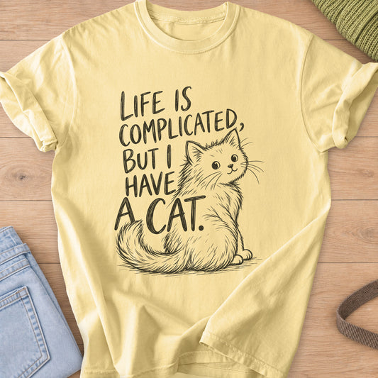Fluffy cat sits and looks back beside "Life is complicated, but I have a cat.", dark charcoal ink on a Butter T-Shirt