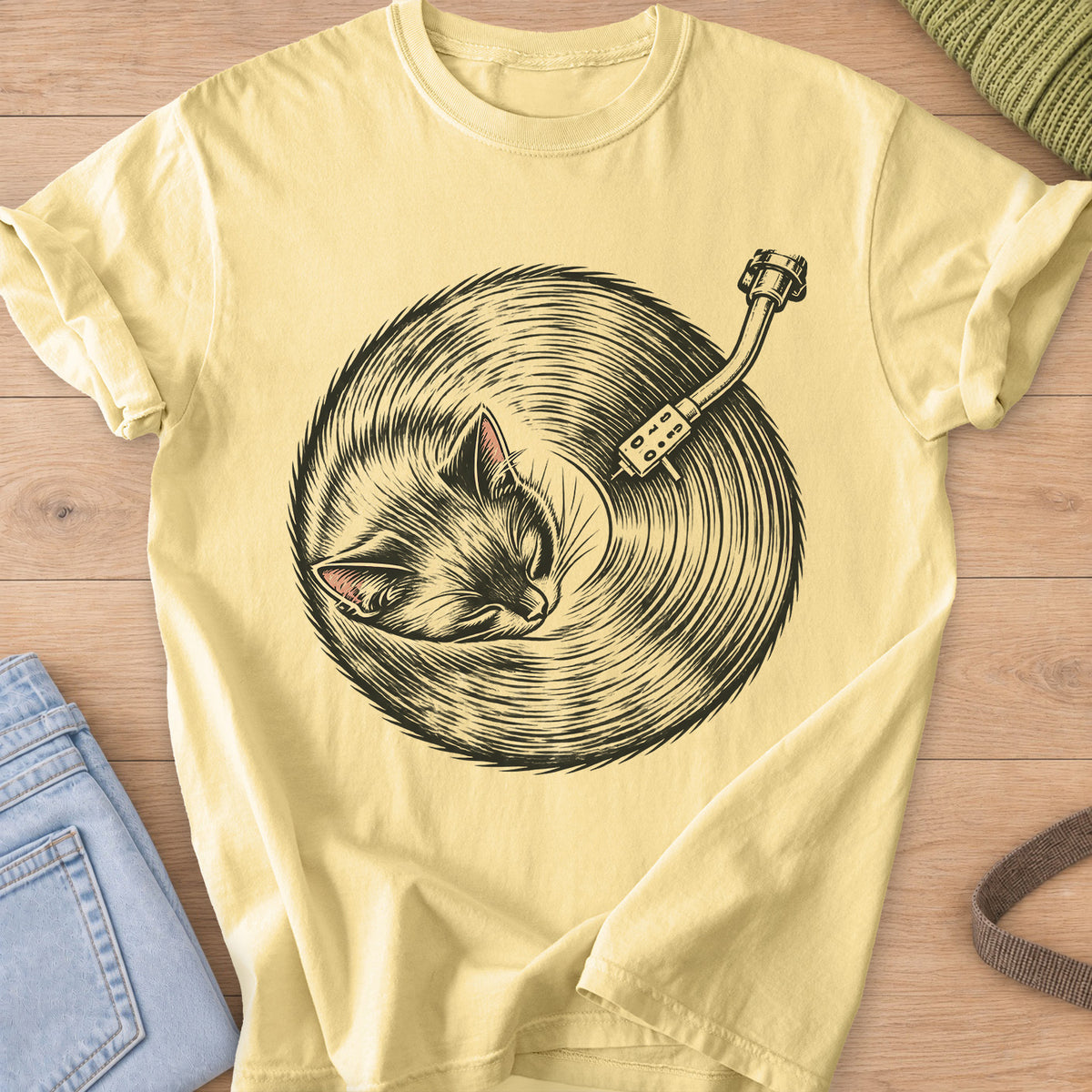 Sleeping cat curled up, its fur forming a vinyl record under a turntable arm, dark charcoal ink on a Butter T-Shirt