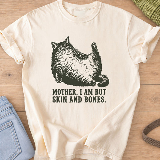 Chubby fluffy cat lying on its back, one paw raised, above "SKIN AND BONES", dark charcoal ink on an Ivory T-Shirt
