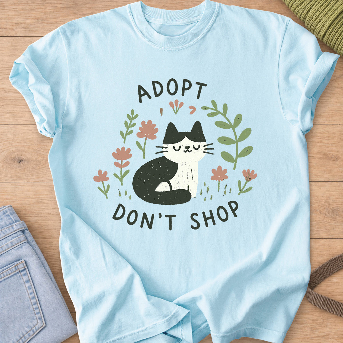 Tuxedo cat sitting with eyes closed among flowers and leaves, "Adopt Don't Shop" on a Chambray T-Shirt