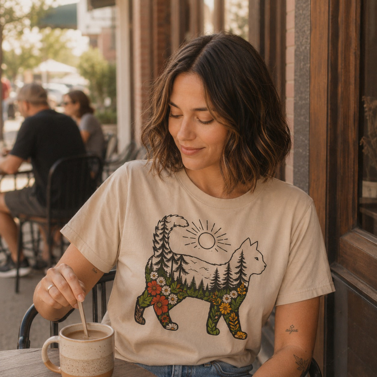 Woman at a cafe wearing the Woodland Cat t-shirt in Sand